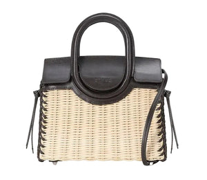 The Staud Maude Mini Wicker Carryall features a woven wicker body, black leather top handle, flap closure, and a sleek shoulder strap—this structured bag is perfect for elevating any look. Shown against a white background.