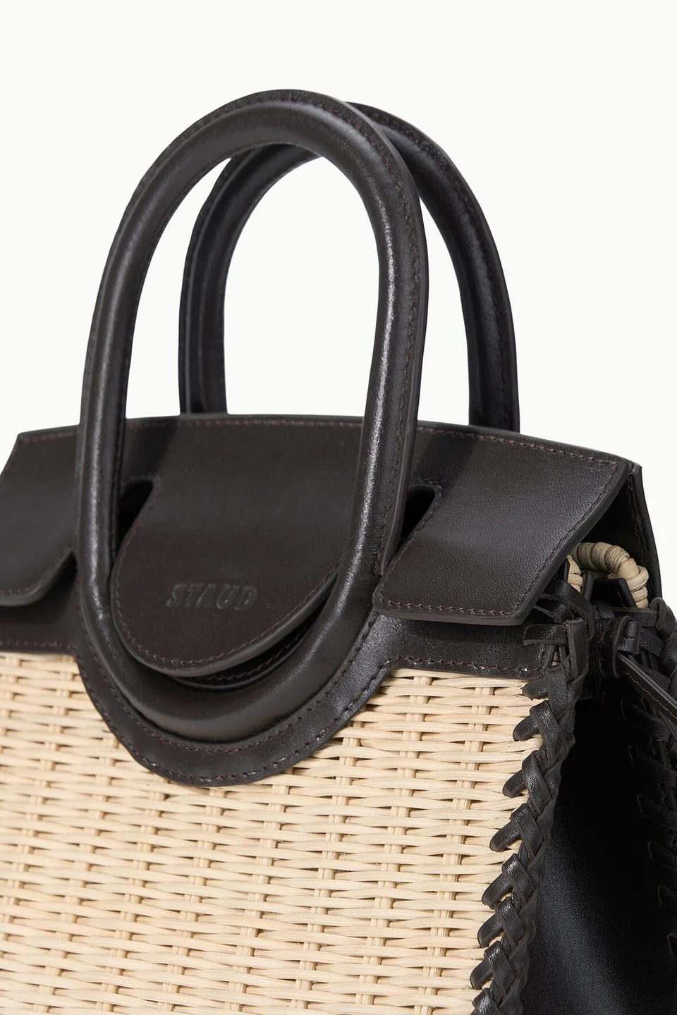 Close-up of the Staud Maude Mini Wicker Carryall, a structured beige and brown leather bag with rounded top handles and visible stitching, highlighting its elegant design.
