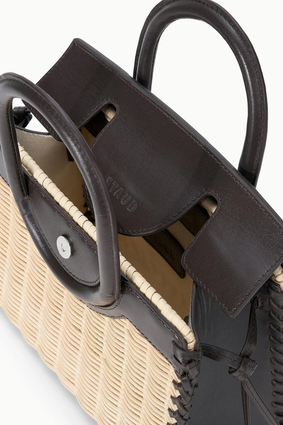 Close-up of the Staud Maude Mini Wicker Carryall, featuring dark brown leather handles, trim, and flap, with an open top that reveals the structured interior of this chic handheld bag.