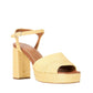 The Staud Jodie Platform Heel is a tan sandal featuring a chunky block heel, platform sole, square toe, wide cross toe strap, ankle buckle strap, and a textured woven finish.
