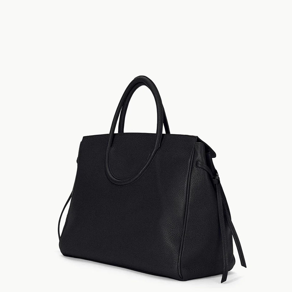 The Staud Maude Carryall is a black pebbled leather tote bag featuring double handles and a structured silhouette, shown against a plain white background. This oversized bag blends timeless style with everyday practicality.