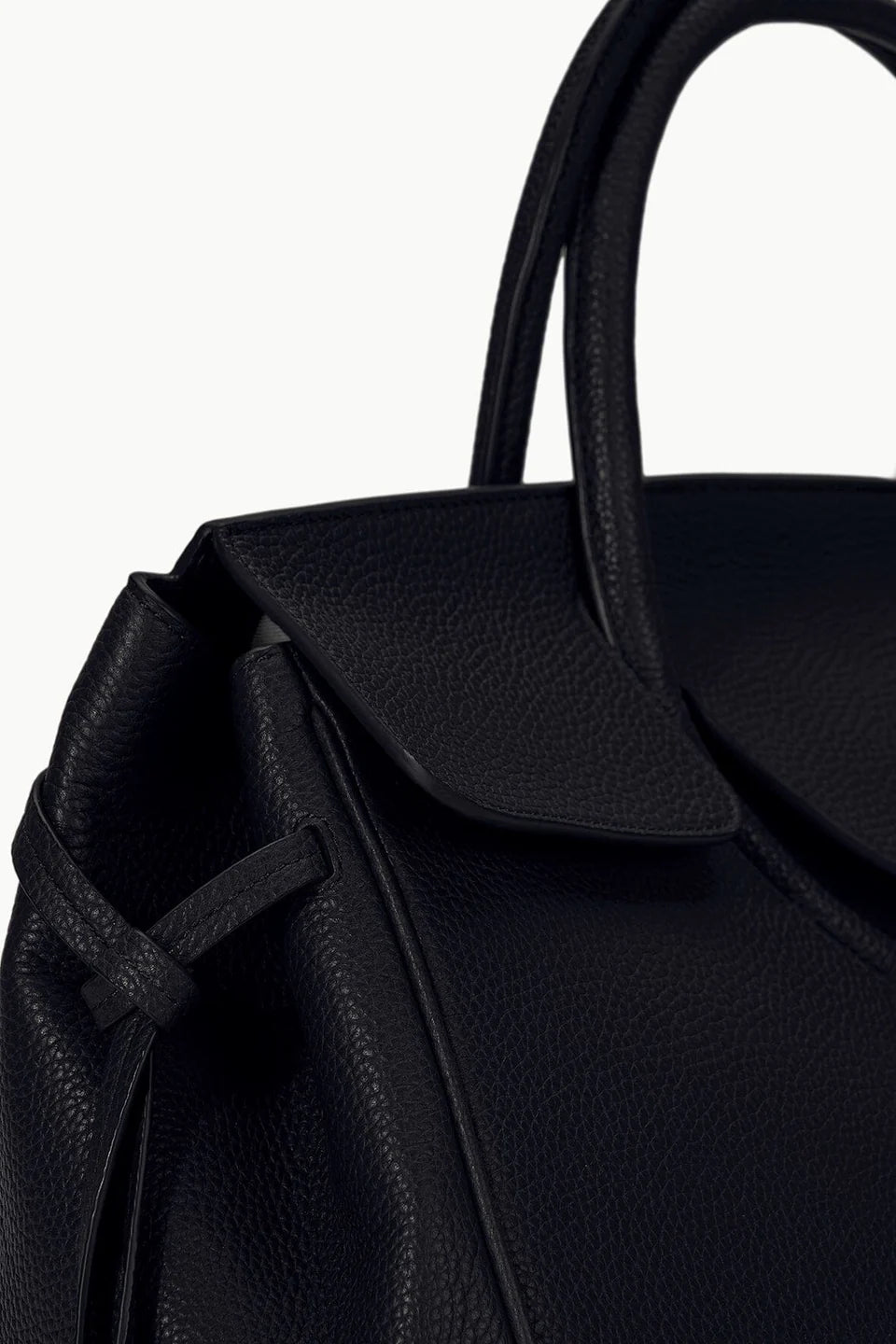 Close-up of the Staud Maude Carryall, a black pebbled leather handbag featuring structured handles and a flap closure, shown against a plain white background.