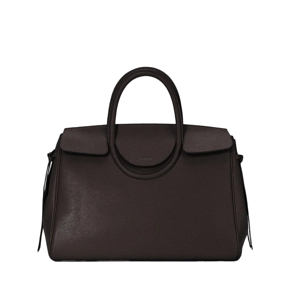 The Staud Maude Carryall is a dark brown pebbled leather handbag featuring a structured shape, top handle, flap closure, and minimal front branding.