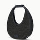 The Staud Moon Raffia Tote Bag is a black, crescent-shaped woven handbag with a short structured handle, magnetic closure, and a small rectangular logo patch on the lower front.