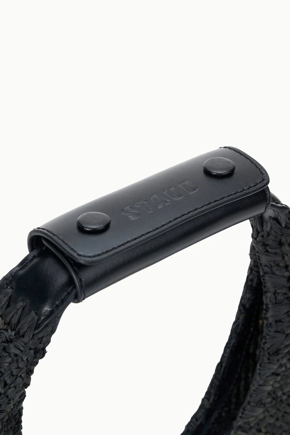 Close-up of a black woven strap with a black leather handle attached by two buttons, embossed with "STAUD"—a stylish detail perfect for your Moon Raffia Tote Bag.