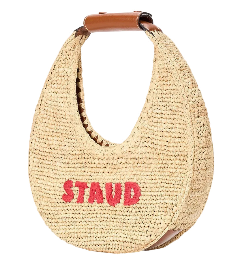 The Staud Moon Raffia Tote Bag features a woven design, brown leather handle, and "STAUD" embroidered in red—ideal as a chic beach accessory for sunny days.