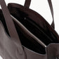 A close-up view of the Staud Piper Tote, an open dark brown leather laptop bag with two shoulder straps, buckle accents, and a visible interior zip compartment.