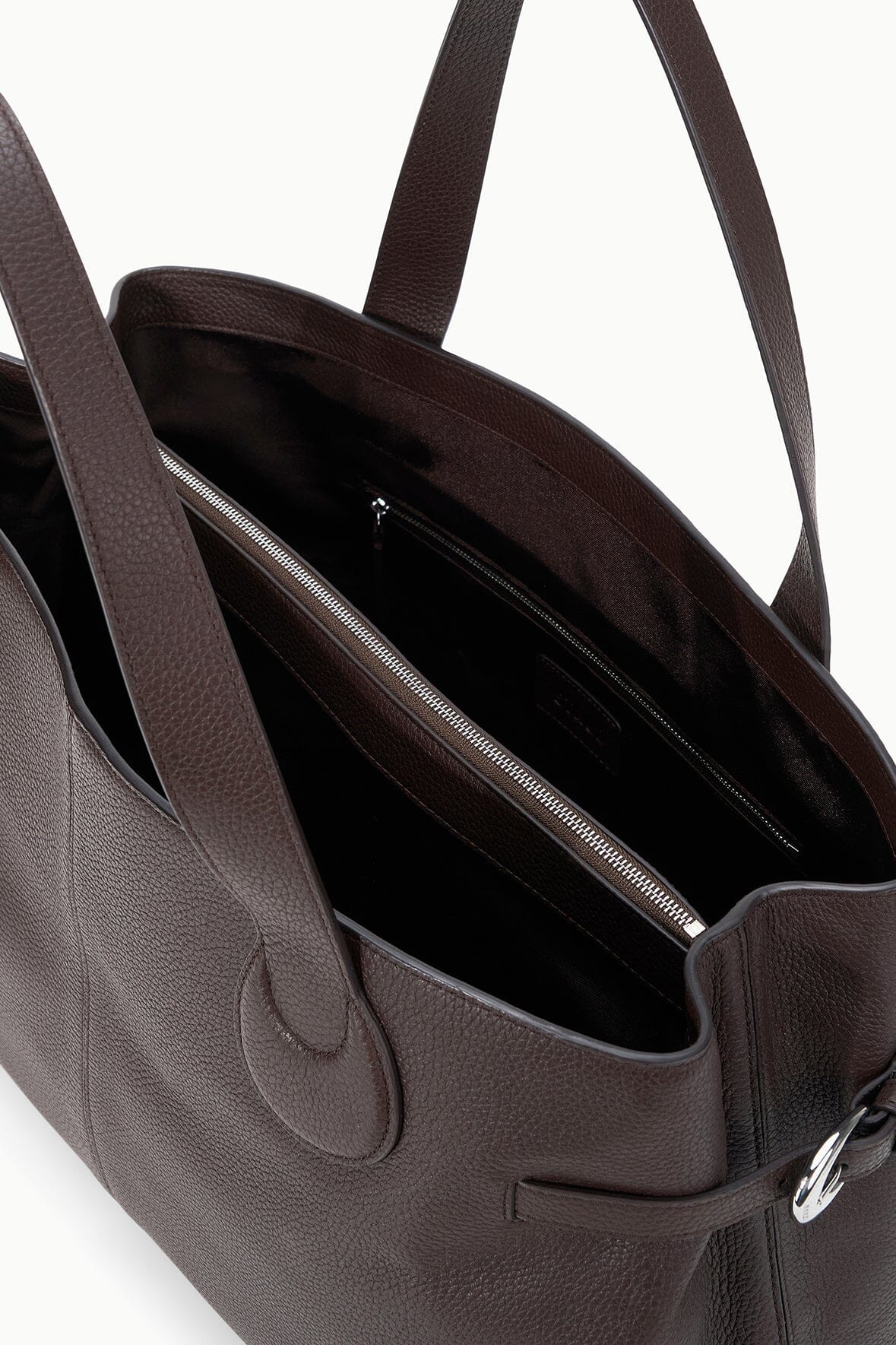 A close-up view of the Staud Piper Tote, an open dark brown leather laptop bag with two shoulder straps, buckle accents, and a visible interior zip compartment.
