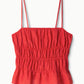 The Ayla Linen Tank by Staud is a red, sleeveless cami featuring thin spaghetti straps, a smocked bodice, and a slightly flared cropped hem, shown against a white background.