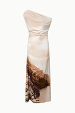 The Staud Phare Silk Maxi Dress is an elegant, ankle-length beige dress crafted from silk, featuring a one-shoulder design and adorned with a landscape print of cliffs and buildings near the water along the lower hem, effortlessly blending timeless style with artistic flair.