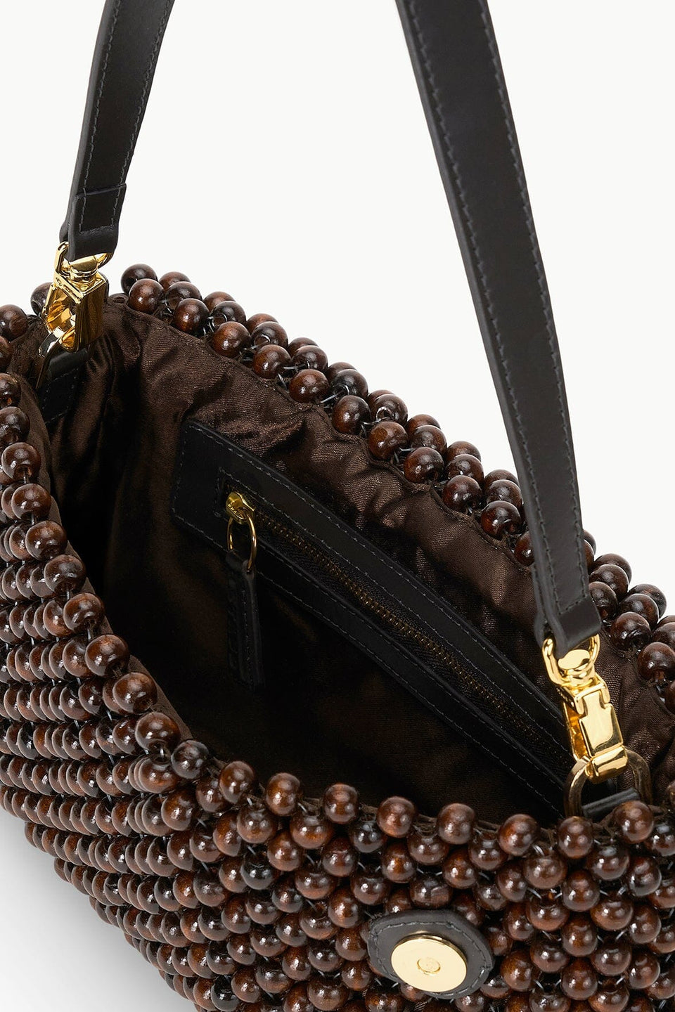 A close-up of the Staud Timmy Convertible Shoulder Bag featuring a brown beaded exterior, black leather strap, gold hardware, and an interior zip pocket.