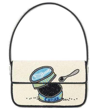 The Staud Tommy Beaded Bag is crafted from vegan leather and features hand-beading with an open caviar tin, small spoon, and caviar on a cream background, finished with a magnetic snap closure.