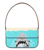 The Staud Tommy Beaded Bag is a rectangular, hand-beaded vegan leather bag with a sequin shark's open mouth in blue water, single strap, and magnetic snap closure.
