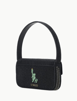 A compact black Tommy Beaded Bag by Staud, made from vegan leather with a textured finish, features an embroidered Statue of Liberty outline and the “STAUD” logo on the front flap, secured with a magnetic snap closure.