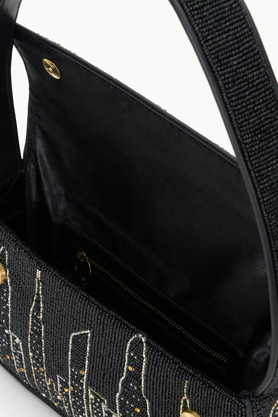 A close-up of the Staud Tommy Beaded Bag, an open vegan leather handbag featuring a city skyline bead design, magnetic snap closure, and a visible interior zip pocket.