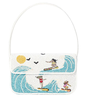 The Staud Tommy Beaded Bag in white vegan leather features three surfers riding waves under a yellow sun with black birds, and closes with a magnetic snap.