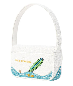 The Staud Tommy Beaded Bag is a white vegan leather bag featuring hand-beaded artwork of a green surfboard on blue waves, with yellow “STICK IT TO THE SWEL” text.