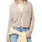 A person wearing the Guest in Residence Stealth Cardigan in beige, blue jeans, a yellow sweater tied at the waist, and a shell necklace.