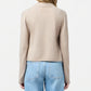 A woman stands facing away, wearing the Stealth Cardigan by Guest in Residence with light blue high-waisted jeans against a plain white background.