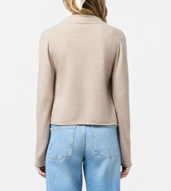 A woman stands facing away, wearing the Stealth Cardigan by Guest in Residence with light blue high-waisted jeans against a plain white background.