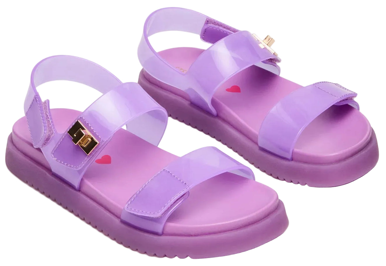 Introducing the Steve Madden Kids Girls’ Jelly Mona Sandal—a stylish pair of purple sandals featuring translucent straps, chic gold buckle accents, and a charming red heart design on the insole. The flatform silhouette offers trendy flair and added comfort, making them perfect for your little fashionista’s all-day adventures.