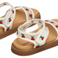 The Steve Madden Kids Toddlers’ Lyla Sandal features a white footbed with embroidered cherry details, brown soles, and adjustable Velcro straps, shown against a plain white background.