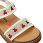 The Toddlers’ Lyla Sandal by Steve Madden Kids features a tan footbed and clear white adjustable Velcro straps adorned with embroidered red cherries and green stems. A pink heart and partial brand text are visible on the insole.