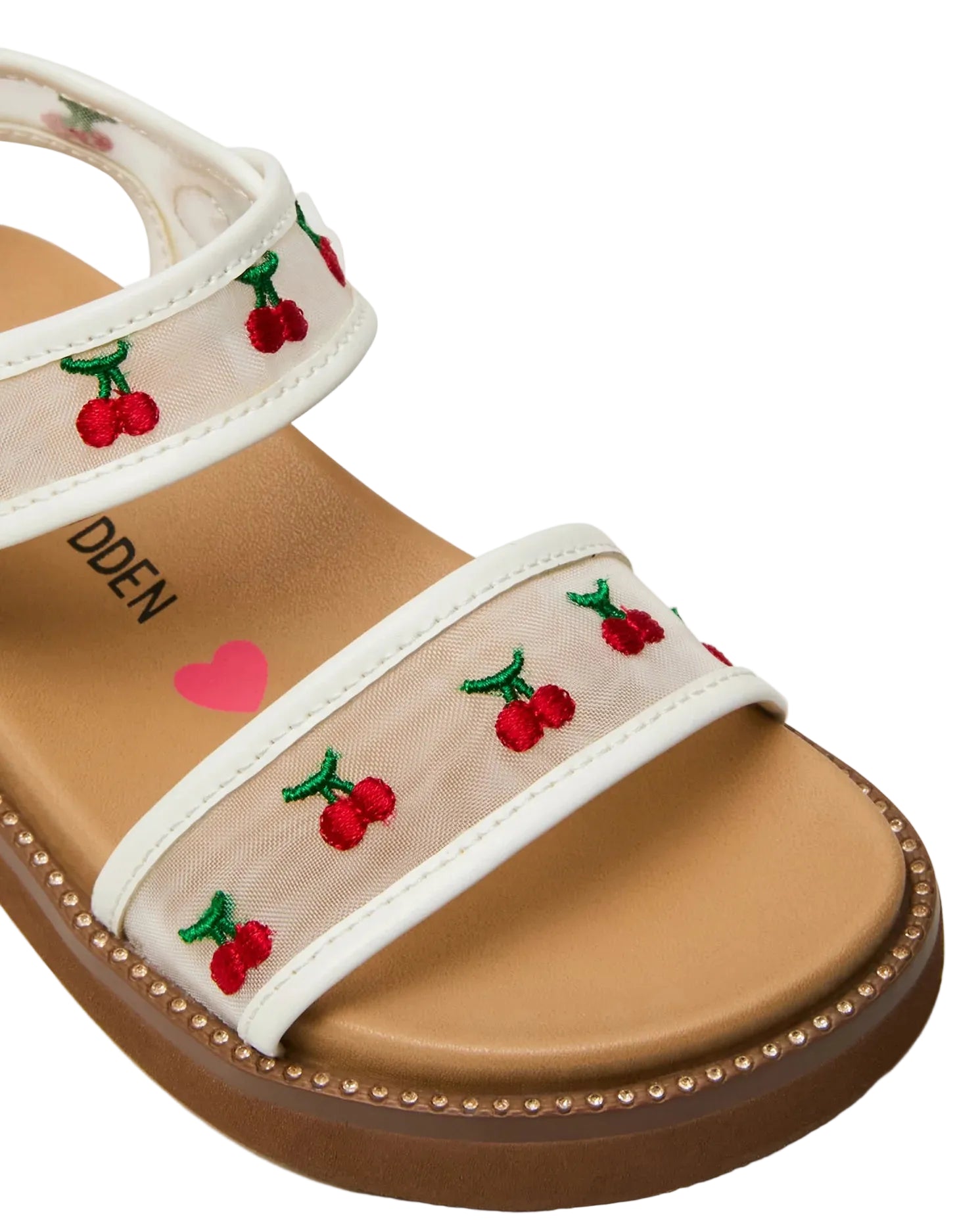 The Toddlers’ Lyla Sandal by Steve Madden Kids features a tan footbed and clear white adjustable Velcro straps adorned with embroidered red cherries and green stems. A pink heart and partial brand text are visible on the insole.