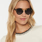 A woman with long blonde hair wears Krewe's STL Nylon Polarized Sunglasses featuring an oversized silhouette, paired with a white top with black trim, against a plain light background.