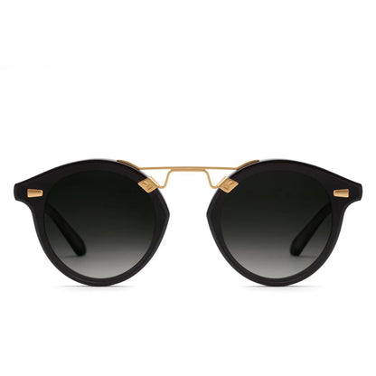 The Krewe STL Nylon Polarized Sunglasses feature an oversized round black frame with gold accents and dark gradient flat nylon lenses, shown on a white background.