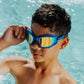 A boy wearing Bling2O Kids' Streamline Goggles in blue and yellow stands in a pool, with wet hair and water droplets on his skin.