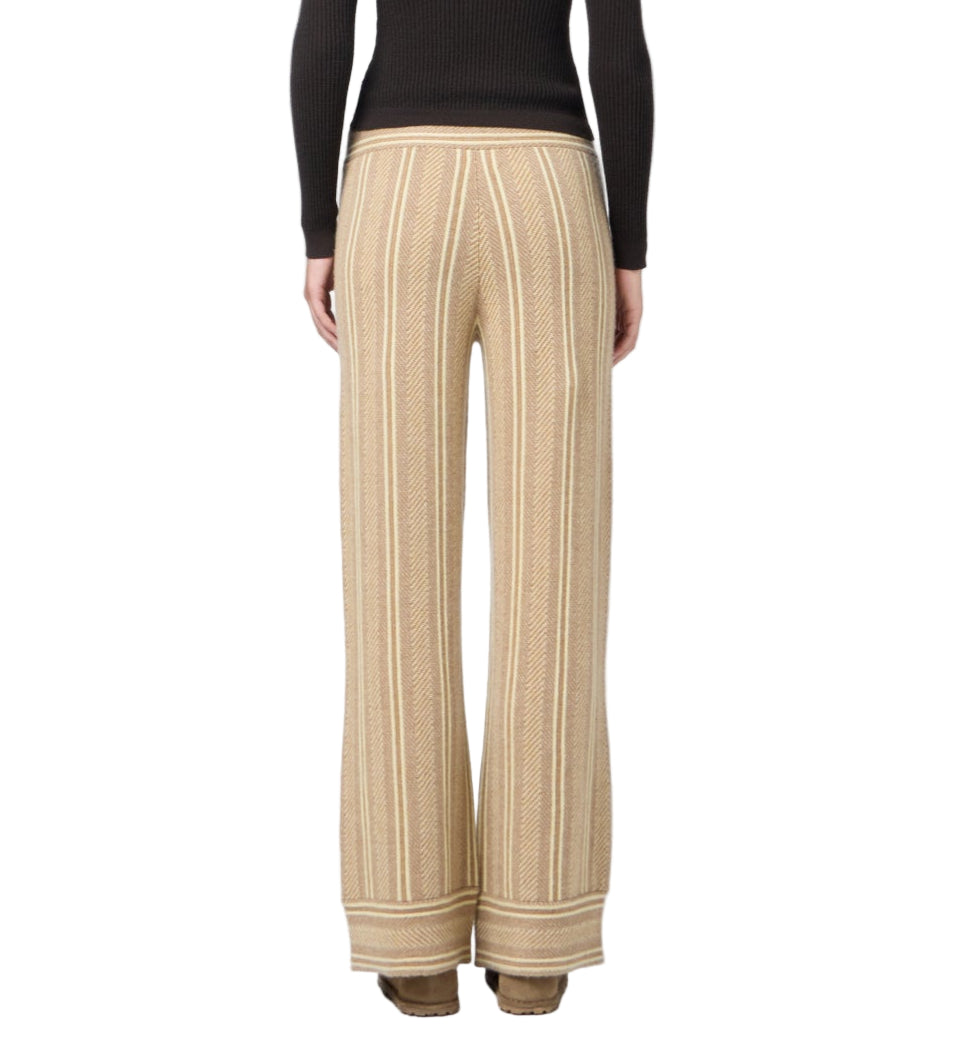 A person is shown from the back wearing the Guest in Residence Stripe Lounge Pant in beige with vertical white stripes, paired with a fitted black long-sleeve top and brown shoes.