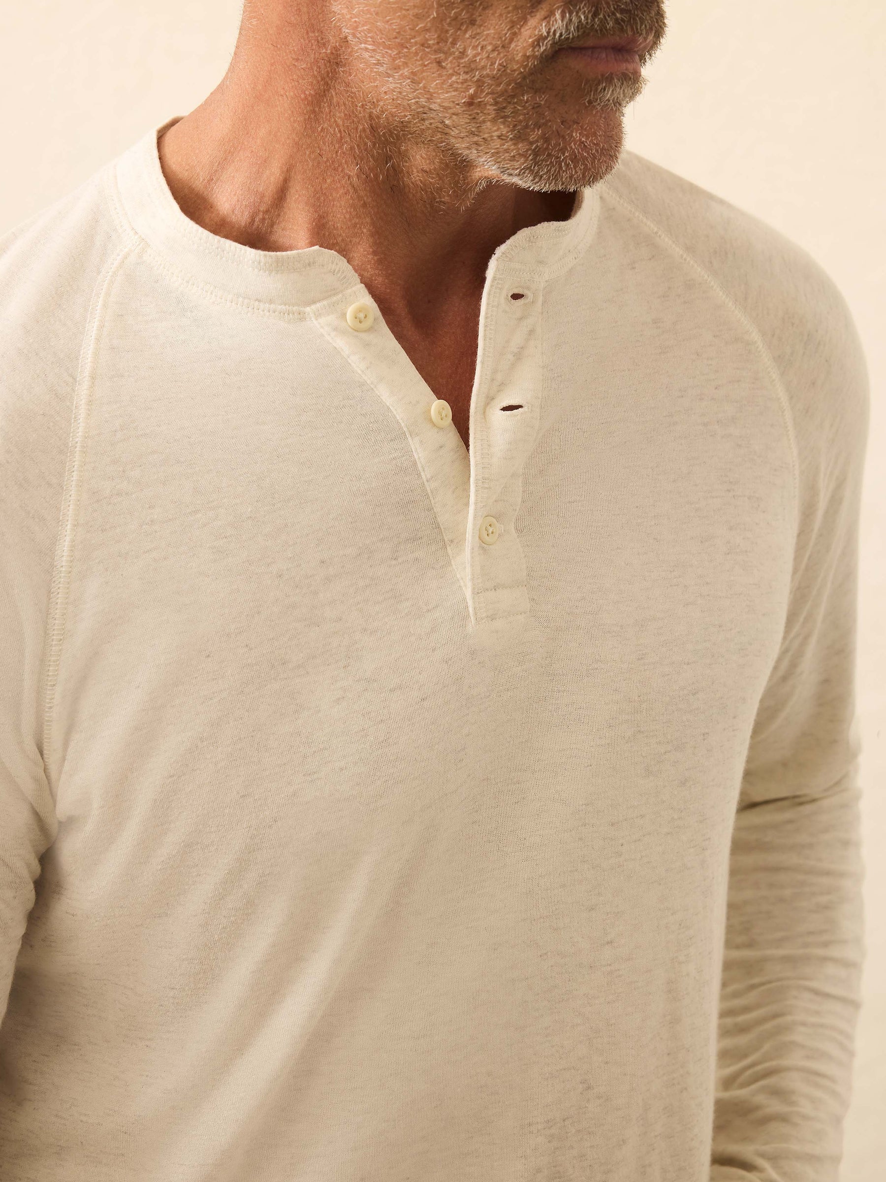 A man wearing a light-colored Faherty Long-Sleeved Cloud Henley with three buttons undone, shown from shoulders to mid-torso.