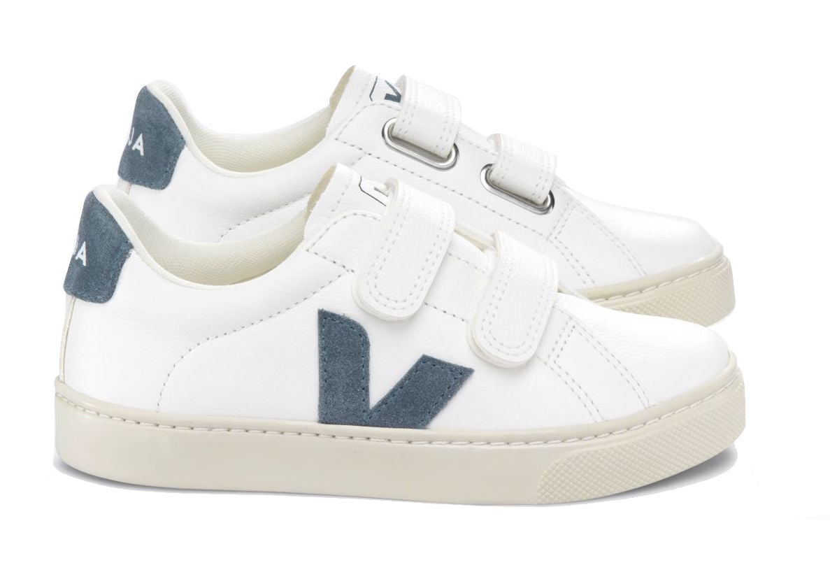 The Veja Junior Esplar Velcro Chromefree Leather Sneaker is a pair of white children’s sneakers featuring two velcro straps, grey accents on the heel and side, and beige soles made from Amazonian rubber.