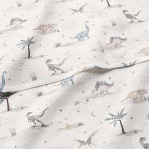 The Gooselings Dino Dreams Swaddle is a 100% cotton blanket adorned with pastel dinosaurs, trees, clouds, and scattered stars on white—an adorable addition to any nursery.