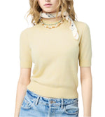 Woman wearing a light yellow Sweater Tee by Guest in Residence, blue jeans, a printed neck scarf, and a beaded necklace.
