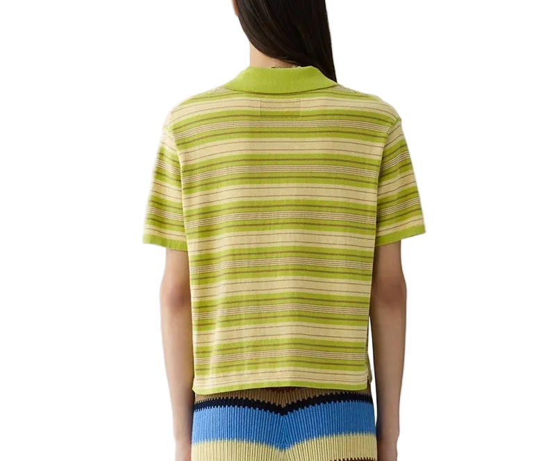 A person is seen from behind, wearing the Guest in Residence Short Sleeve Stripe Rugby in green and yellow over a cotton-cashmere tee, paired with a pleated color-block skirt in blue, yellow, and black.