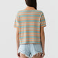 Person standing with their back to the camera, wearing the Guest in Residence Short Sleeve Stripe Rugby in orange and blue, and light blue frayed denim shorts against a white background.