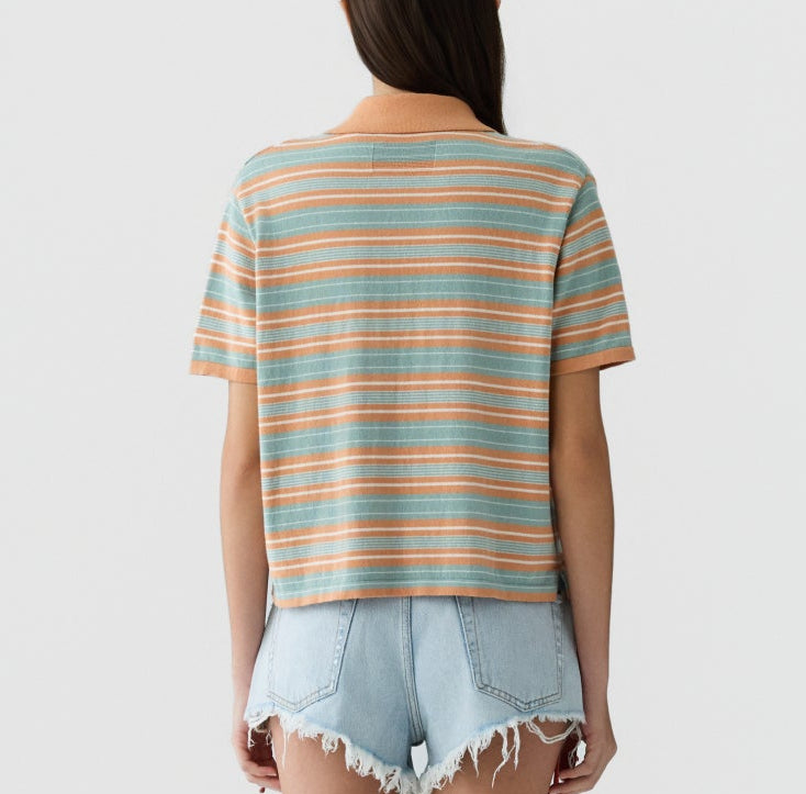 Person standing with their back to the camera, wearing the Guest in Residence Short Sleeve Stripe Rugby in orange and blue, and light blue frayed denim shorts against a white background.