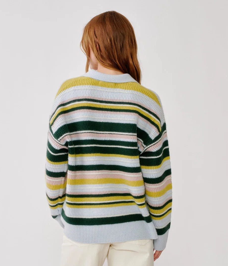 A person with long, reddish hair is seen from behind against a plain white background, wearing the Billie Sweater by Sablyn—a loose cashmere sweater featuring green, yellow, white, and pale pink stripes.