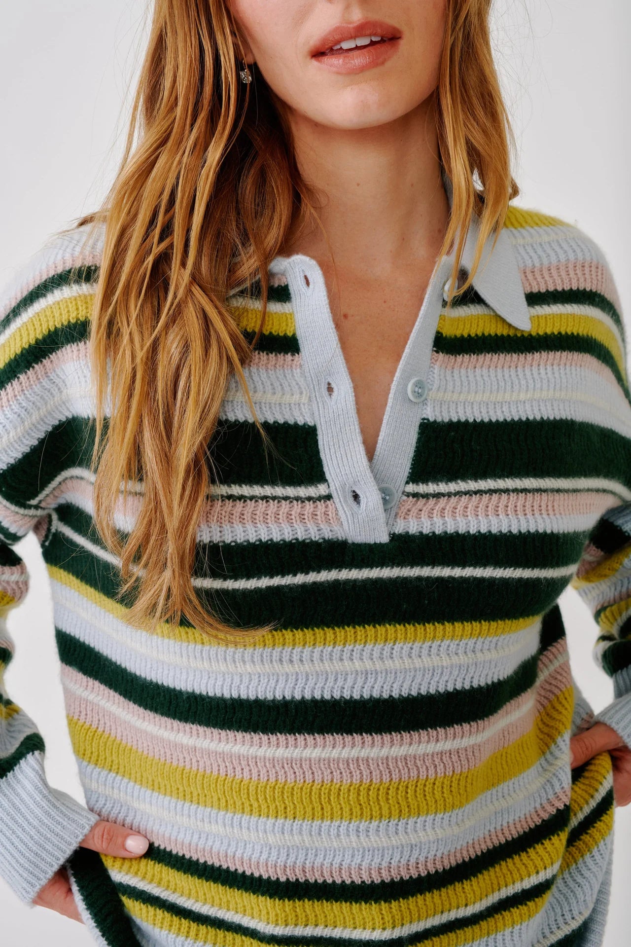 A woman with long, wavy hair wears the Sablyn Billie Sweater, featuring a collared design and horizontal stripes in green, white, pink, yellow, and blue. She stands against a plain white background.