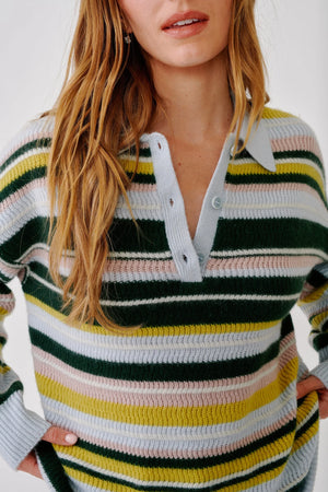A woman with long, wavy hair wears the Sablyn Billie Sweater, featuring a collared design and horizontal stripes in green, white, pink, yellow, and blue. She stands against a plain white background.