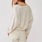 A person wearing the Sablyn Koda Wrap Cashmere Sweater—an oversized off-white wrap-front style with a deep V neckline—paired with cream pants stands facing away, highlighting the back and side of the outfit against a plain light background.