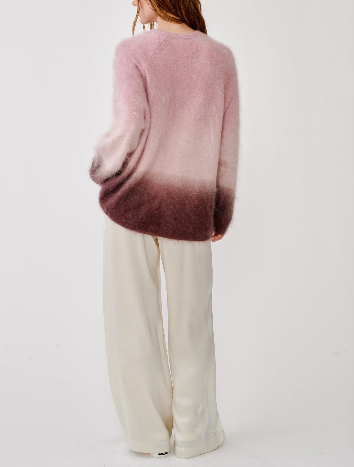 A person is seen from behind wearing the Sablyn June Ombre Crewneck Sweater, featuring a fuzzy pink and burgundy ombré finish, paired with loose white pants against a plain white background.