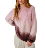 A woman wearing the Sablyn June Ombre Crewneck Sweater—a fuzzy, long-sleeve sweater with a pink-to-burgundy ombré finish—paired with white pants, standing against a white background.