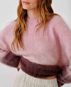 A woman models the Sablyn June Ombre Crewneck Sweater—a fuzzy, color-blocked raglan style in pink and burgundy—paired with loose cream pants, shown from shoulders to hips against a plain background.
