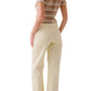 A woman stands with her back to the camera, wearing the Sablyn Jude Short Sleeve Tee with multicolor stripes, cream high-waisted pants, and sandals.