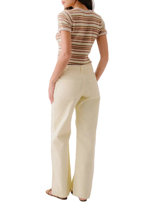 A woman stands with her back to the camera, wearing the Sablyn Jude Short Sleeve Tee with multicolor stripes, cream high-waisted pants, and sandals.