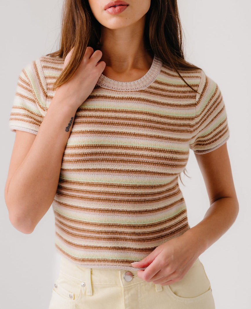 A woman wears the Sablyn Jude Short Sleeve Tee, featuring beige, brown, and cream multicolor stripes, paired with light pants against a plain background.