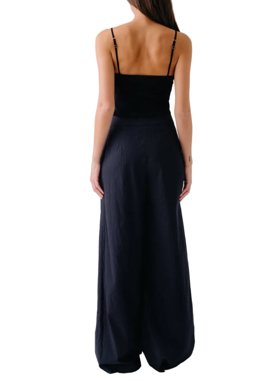A woman is shown from the back wearing the Sablyn Ada V-Neck Cami with Lace, featuring thin straps and delicate trim, paired with high-waisted wide-leg black pants.